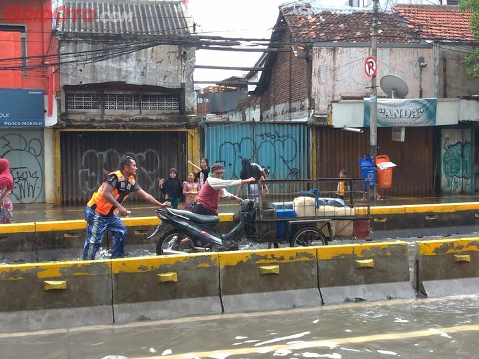 Seorang petugas Satpol PP mendorong gerobak motor yang mogok akibat menerjang banjir.
