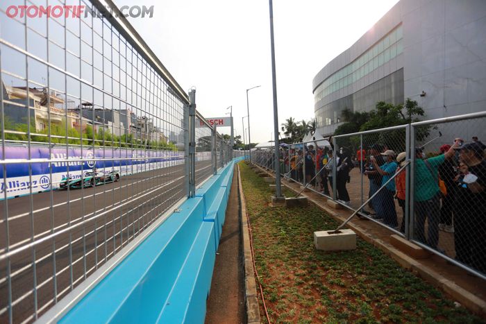 Para penonton antusias mengabadikan dengan ponsel dari balik pagar kawat.