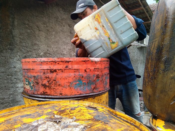 Seorang mekanik tengah mengumpulkan sisa oli bekas di drum.