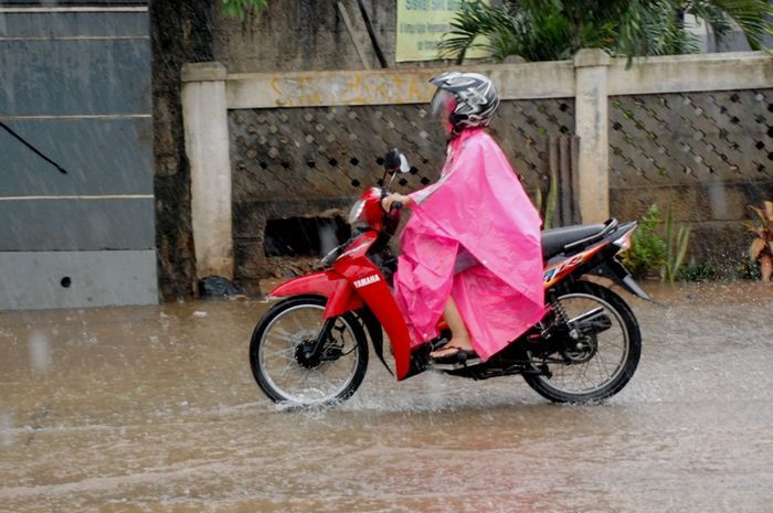 Ilustrasi naik motor saat hujan, tidak dianjurkan pakai jas hujan ponco dan sendal jepit