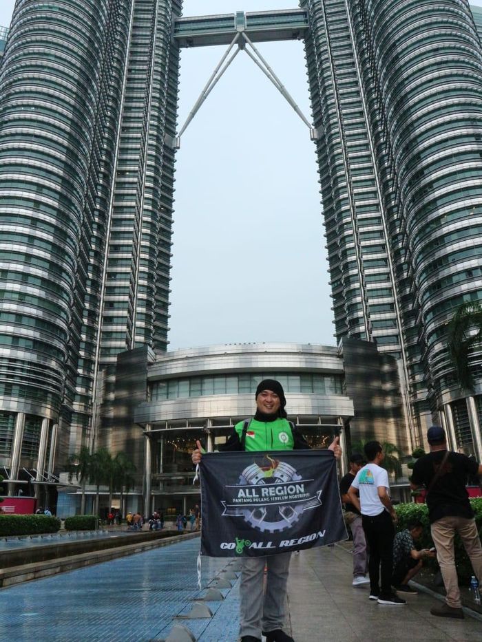 Alfian Ronald pose di depan menara kembar Petronas sembari bawa bendera komunitas Gojek All Region 
