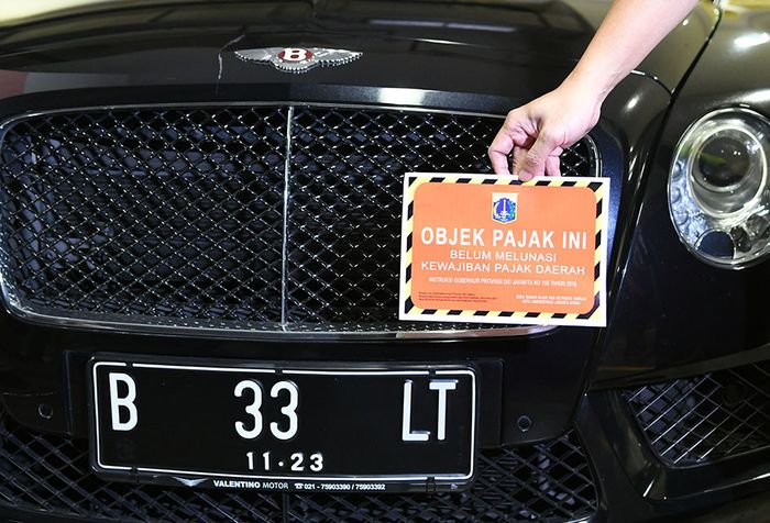 Petugas Samsat Jakarta Utara menunjukkan stiker 'Objek Pajak' di depan mobil mewah Bentley saat razia supervisi pencegahan pajak mobil mewah di Apartemen Regatta, Jakarta Utara di Jakarta, Kamis (5/12/2019). Badan Pajak dan Restribusi Daerah (BPRD) DKI Jakarta bekerja sama dengan Samsat Jakarta Utar