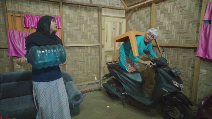 Beti menuruti Mak Beti sambil mengangkat galon kosong