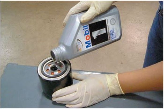 Ilustrasi memasukkan oli mesin ke dalam filter oli yang baru sebelum dipasang