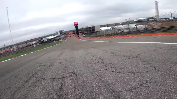 Permukaan aspal COTA yang bergelombang dan retak-retak di tikungan pertama.