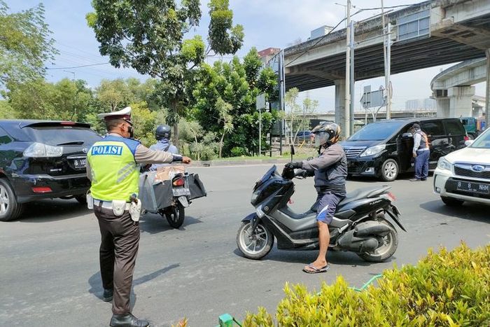 Seorang polantas mengarahkan pengendara motor berpelat genap agar putar balik karena aturan ganjil genap di jalan arah wisata Ancol, Jakarta Utara, Sabtu (23/10/2021).