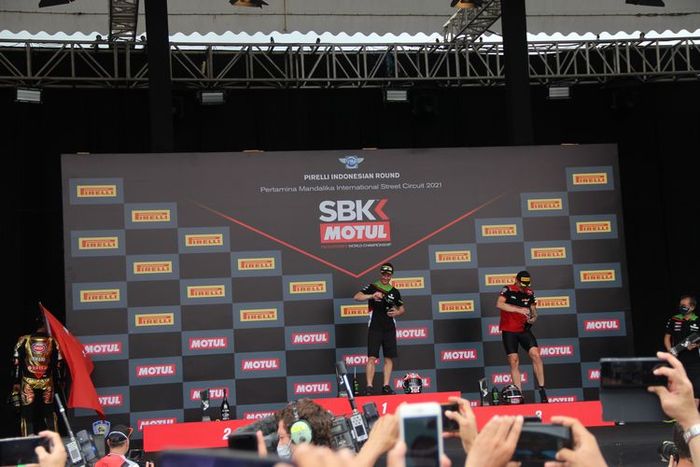 Momen Toprak Razgatlioglu (kiri) berjalan ke balik panggung saat Jonathan Rea (tengah) dan Scott Redding (Kanan) semprot sampanye di podium Race 1 WSBK Indonesia 2021