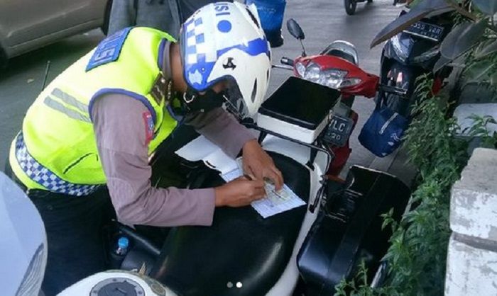 Petugas Kepolisian menulis surat tilang manual ke pelanggar lalu lintas