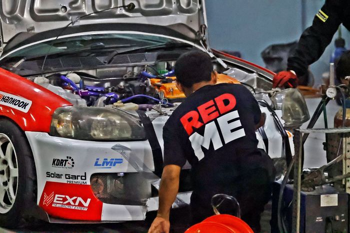 Kru tim Redme Banteng Motorsport x Kurang Dana Racing Team mencoba memperbaiki kerusakan mobil mereka di pit.