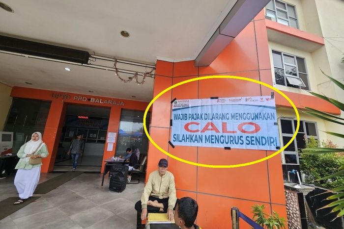Dalam lingkaran kuning, tertempel spanduk bertuliskan 'WAJIB PAJAK DILARANG MENGGUNAKAN CALO, SILAHKAN MENGURUS SENDIRI' di Samsat Balaraja, Tangerang, Banten