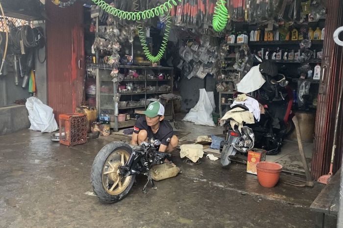 Teguh memperbaiki mesin Yamaha Lexi 125 milik pelanggan usai bengkelnya tersapu air bah imbas jebolnya tembok gudang Dinas SDA di Jl AUP Rawa Minyak, Pasar Minggu, Jakarta Selatan, (21/5/25)
