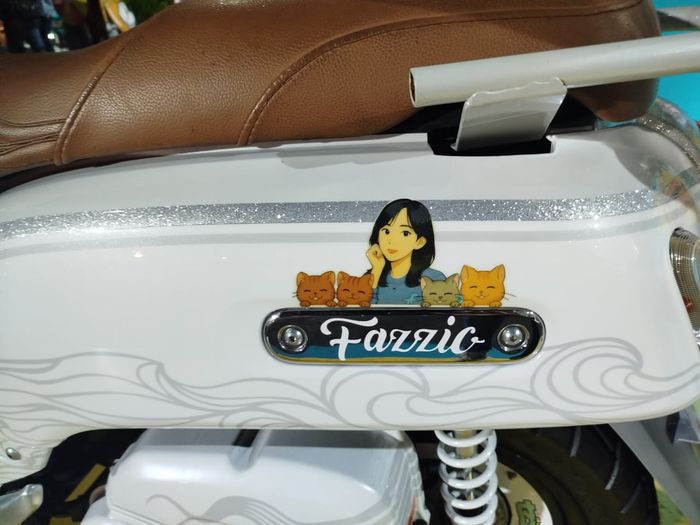 Stiker yang menggambarkan Zee Asadel dan keempat kucingnya menempel di bodi samping Yamaha Fazzio miliknya