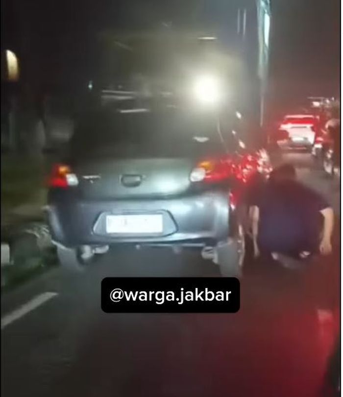 Pengemudi Mitsubishi Mirage menepi mengganti ban yang pecah akibat menghantam lubang jalan di flyover Pesing, Jalan Daan Mogot, Jakarta Barat