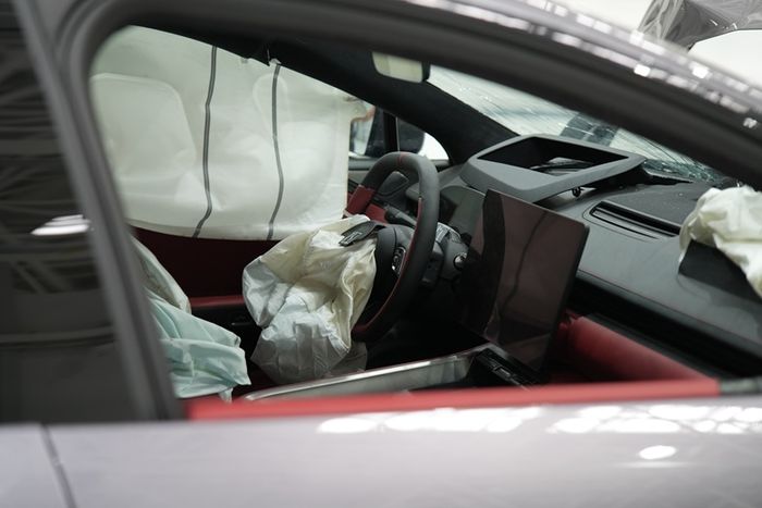 Interior mobil saat uji tabrak terlihat dengan airbag mengembang di area kemudi dan penumpang depan sebagai bagian dari simulasi keselamatan.
