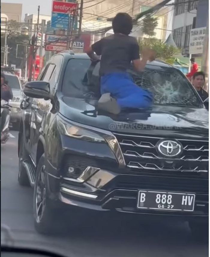 Salah satu warga menaiki kap mesin Toyota Fortuner dan menghantam kaca dengan batu hingga pecah di Jalan KH Mas Mansyur, Tanah Abang, Jakarta Pusat