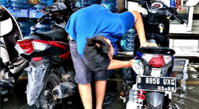 Pria memanfaatkan air yang melimpah untuk membersihkan motornya
