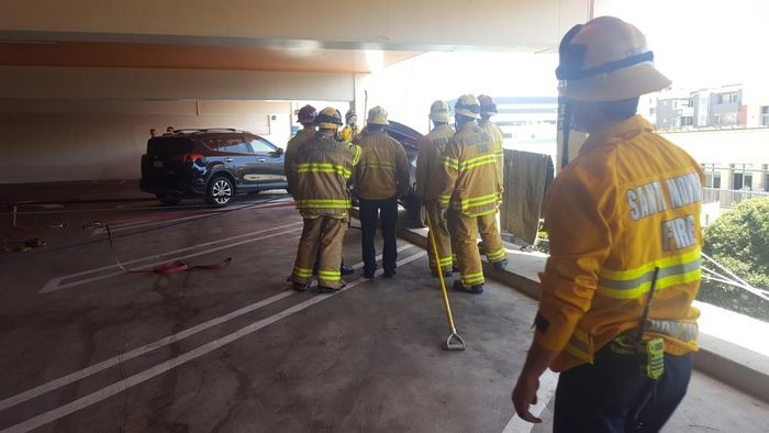 Petugas pemadam kebakaran yang mencoba mengevakuasi mobil yang hampir jatuh dari tempat parkir