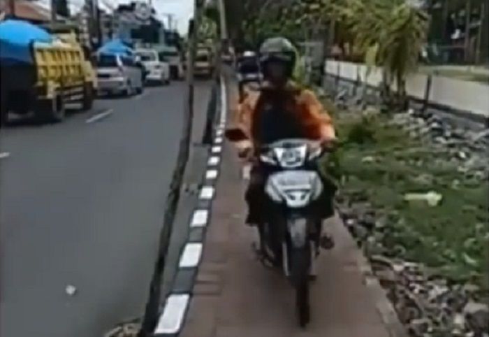 Ilustrasi pemotor yang melintas di trotoar.