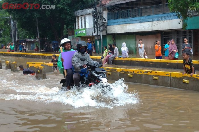 Pengendara motor menerjang banjir sambil berboncengan.