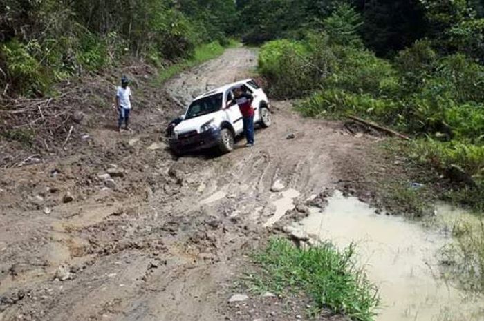 Sebuah mobil mencoba menerobos ruas jalan yang mengalami kerusakan parah di sebuah hutan di Kabupate