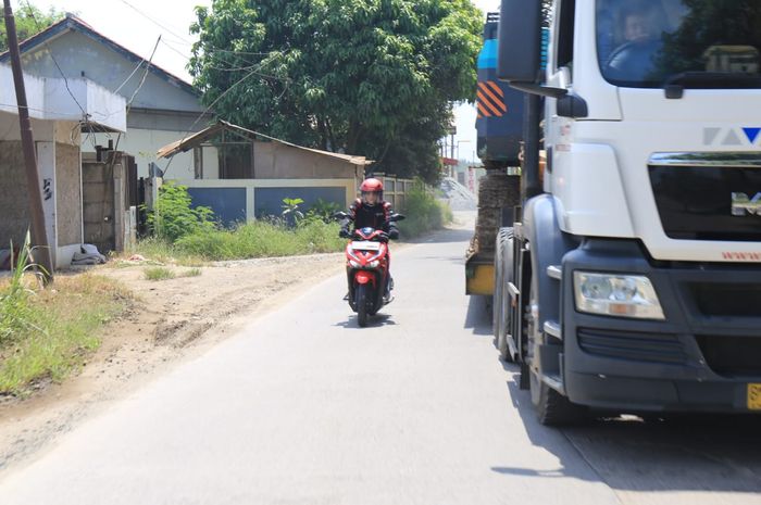 Ilustrasi pengendara motor mendahului kendaraan besar di jalan raya