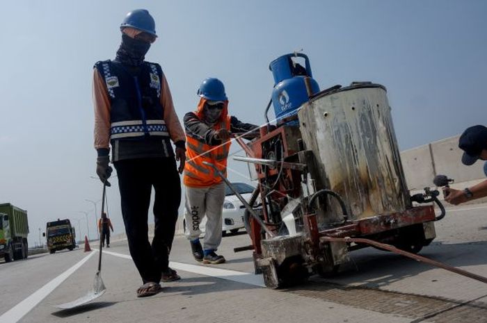 Pekerja yang sedang membuat marka atau garis di jalan raya.