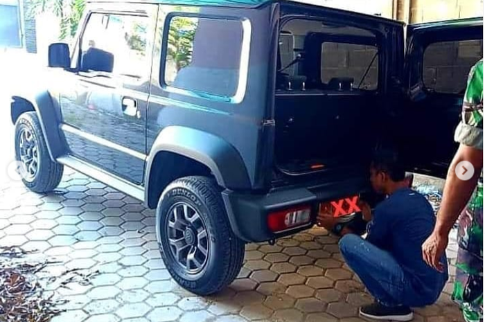 Dua orang salah satunya bersergam TNI memasang pelat nomor Mabes TNI di Suzuki New Jimny