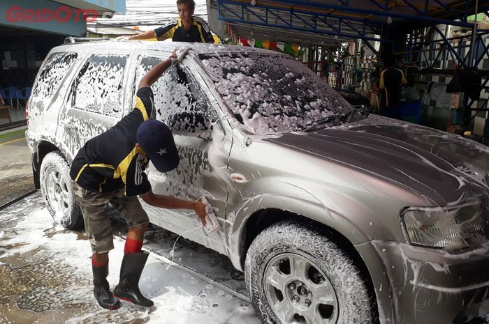 Beberapa petugas di tempat pencucian mobil terlihat sedang mencuci mobil.