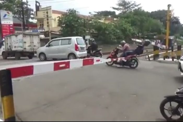 Pemotor nekat menyebrangi pintu rel kereta api yang menutup, tak sadar boncenger tersangkut