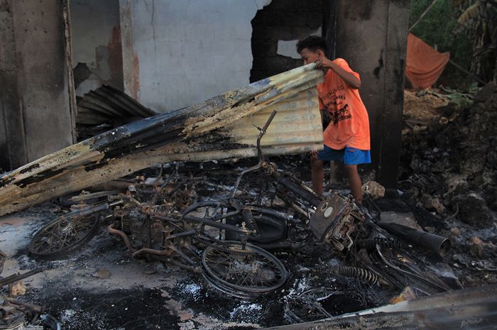 Seorang warga berada di bangkai dua unit sepeda motornya yang terbakar di dalam rumahnya pasca-keributan antar pemuda di Desa Gunung Jaya, Buton, Sulawesi Tenggara, Kamis (6/6/2019).  Pihak kepolisian belum mengetahui jumlah kendaraan yang terbakar pasca-kejadian pembakara.