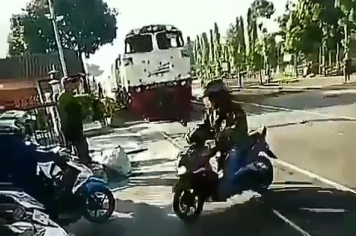 Seorang pengendara matik hitam nekat menyeberangi rel kereta api saat kereta sudah dekat.