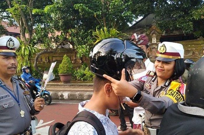Ilustrasi - Polisi saat memberikan helm kepada pengendara yang menggunakan pakaian ibadah dan tidak menggunakan helm di Tabanan, Bali, Kamis (2/5/2019). 