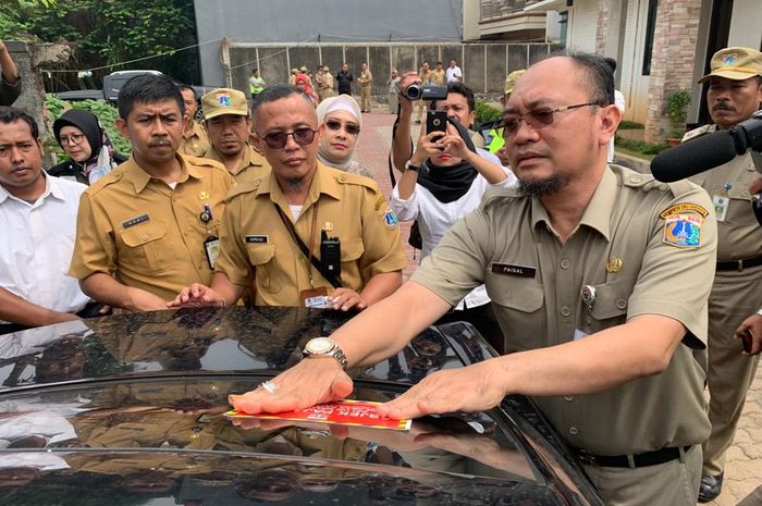 Faisal Syafruddin selaku Kepala BPRD DKI Jakarta menempelkan stiker peringatan di kaca mobil Chrysler 300C