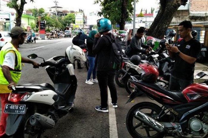Seorang juru parkir membantu mengeluarkan motor pengendara seusai diparkir di Jalan Dr Lukmonohadi, seberang RSUD Kudus, Jawa Tengah