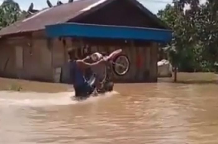 Seorang pemuda lakukan Wheelie dengan motornya di kondisi banjir