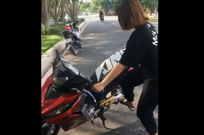 Seorang wanita mempraktekan cara memposisikan standar tengah motor dengan teknik yang mudah dan sederhana.