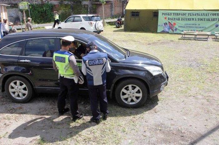 Petugas melakukan pemeriksaan terhadap kendaraan dengan plat nomor luar wilayah yang melintas memasuki perbatasan di Posko Terpadu Penanganan Covid-19 jalan raya Yogyakarta-Magelang, Tempel, Sleman, DI Yogyakarta, Minggu (12/4/2020). Petugas memberhentikan dan mendata asal dan tujuan penggendara, memeriksa suhu tubuh dan memeriksa penggunaan masker 