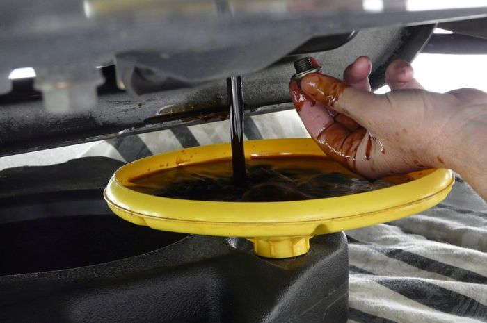 Ilustrasi membuang oli mesin dengan membuka baut pembuangan oli atau drain plug