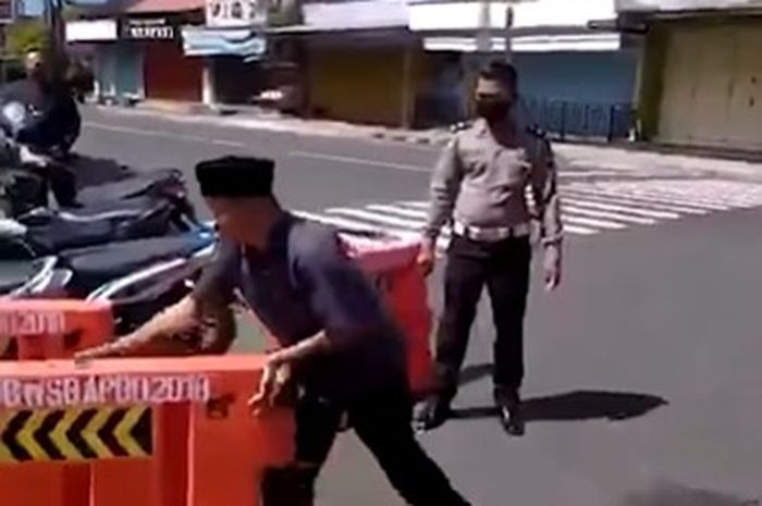 Seorang pria sedang membongkar pembatas jalan di depan polisi