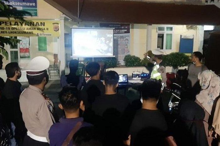 Pelanggar lalu lintas roda dua, disungguhi video kasus pengguna helm yang selamat dari laka lantas, di Pos Kota Simpang Jam, Kecamatan Banda Sakti, Lhokseumawe, Sabtu (4/7/2020). 