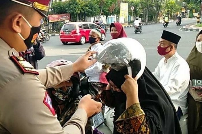 Personel Satlantas Polresta Denpasar tengah membagikan puluhan helm ke pengendara motor saat Hari Raya Idul Adha 1441 H, Jumat (31/07/2020).
