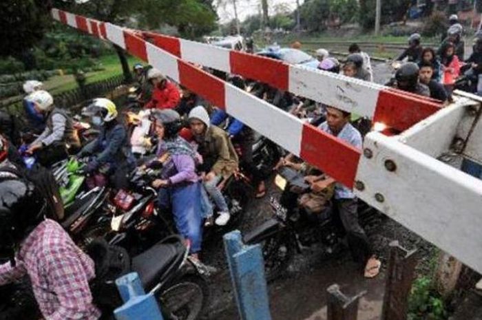 Para pemotor berbondong-bondong melewati pintu perlintasan kereta api.