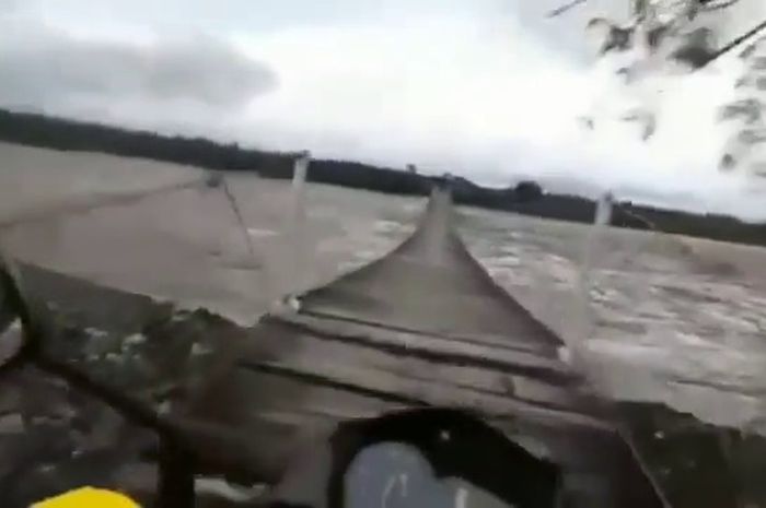 Tangkapan layar seorang pengendara sedang melewati jembatan kayu di saat sungai sedang meluap.