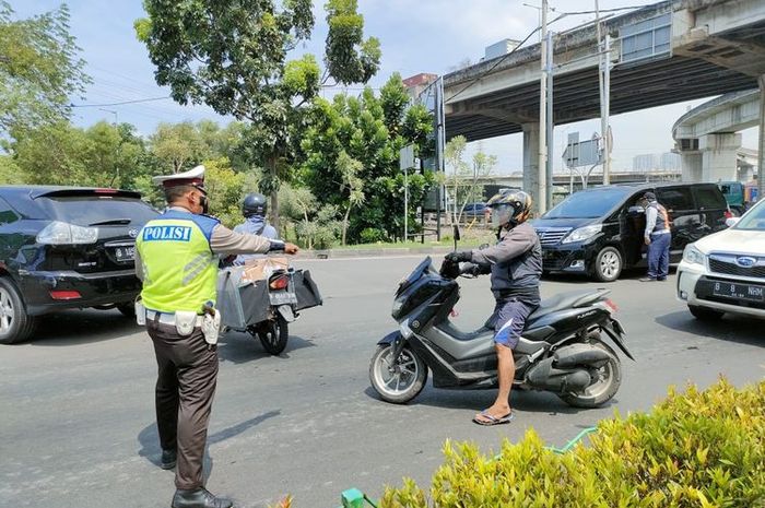 Seorang polantas mengarahkan pengendara motor berpelat genap agar putar balik karena aturan ganjil genap di jalan arah wisata Ancol, Jakarta Utara, Sabtu (23/10/221).