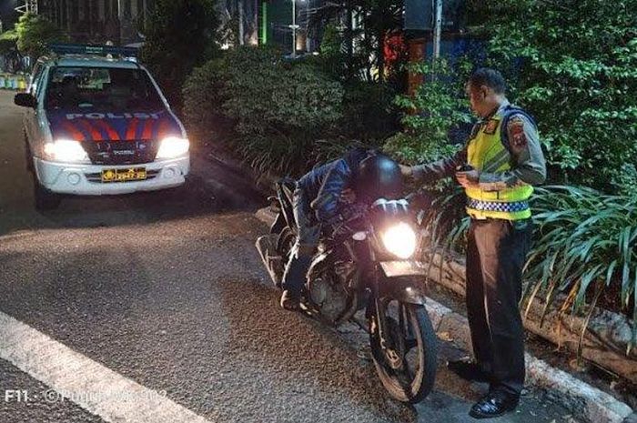 Petugas kepolisian saat membangunkan pemotor yang tertidur di atas motor dengan mesin menyala di Jalan Wonokromo Kota Surabaya.