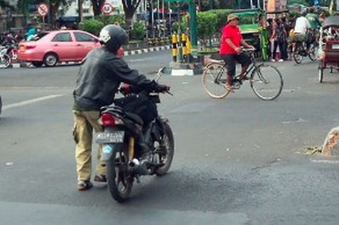 Ilustrasi seseorang menuntun motor mogok di jalan.