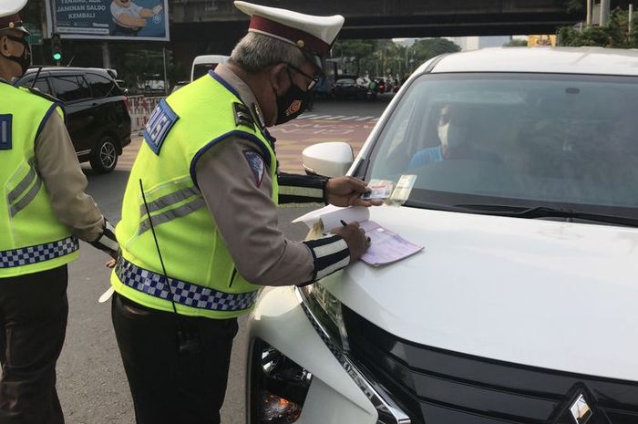 Anggota kepolisian memberikan sanksi tilang untuk mobil yang melanggar sistem ganjil genap di Jalan RS Fatmawati, Cilandak, Jakarta Selatan (25/10/21) pagi.