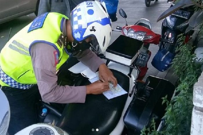 Petugas Kepolisian menulis surat tilang manual ke pelanggar lalu lintas