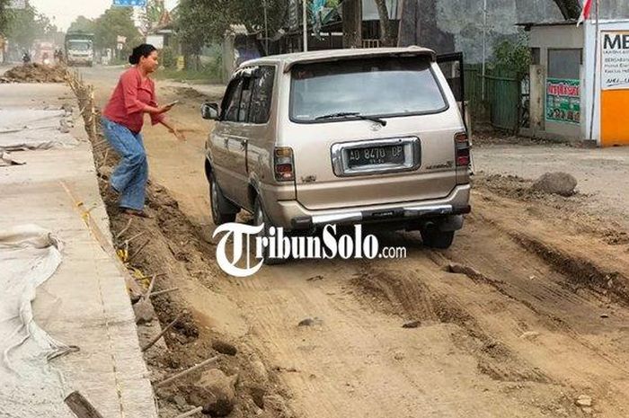 Mobil tersangkut di gundukan tanah di Jalan Raya Solo-Purwodadi yang baru diperbaiki. 