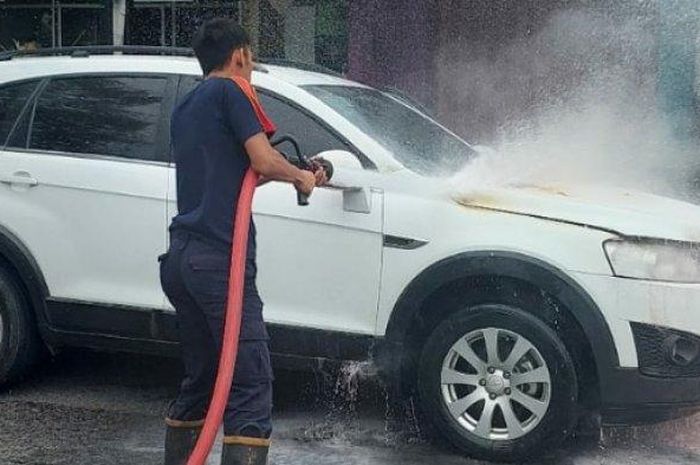 Petugas pemadam kebakaran menyemprotkan air ke arah kap mesin Chevrolet Captiva yang terbakar hingga bikin kap mesin menguning